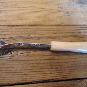 May include: A silver tracing wheel with a white plastic handle. The wheel has a serrated edge and the handle has the words "Dritz Tracing Wheel" printed on it.