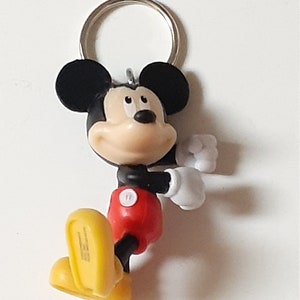 May include: A black and yellow Mickey Mouse keychain with a red shirt and white gloves. The keychain has a silver ring.