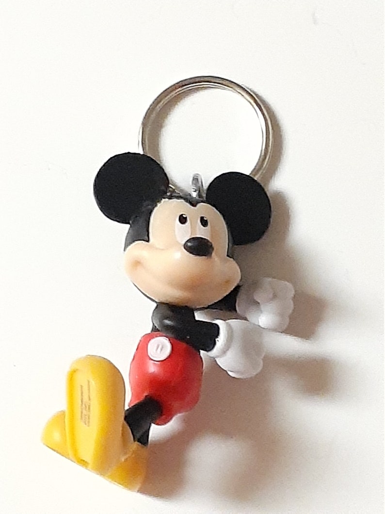 May include: A black and yellow Mickey Mouse keychain with a red shirt and white gloves. The keychain has a silver metal ring.