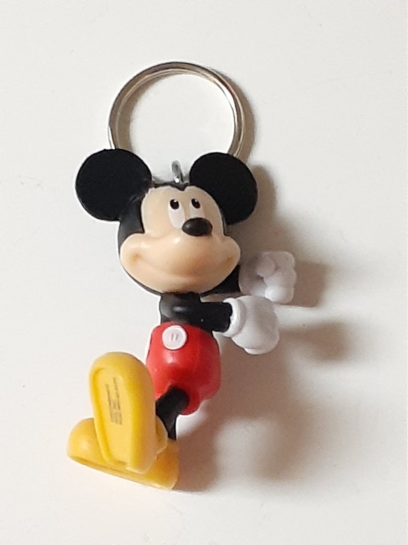 May include: A black and yellow Mickey Mouse keychain with a red shirt and white gloves. The keychain has a silver ring.