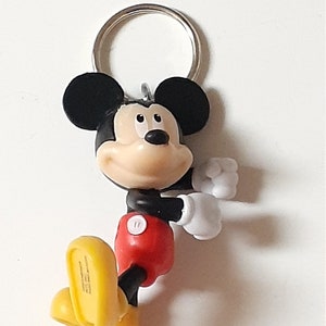 May include: A black and red Mickey Mouse keychain with a yellow shoe. The keychain has a silver metal ring.