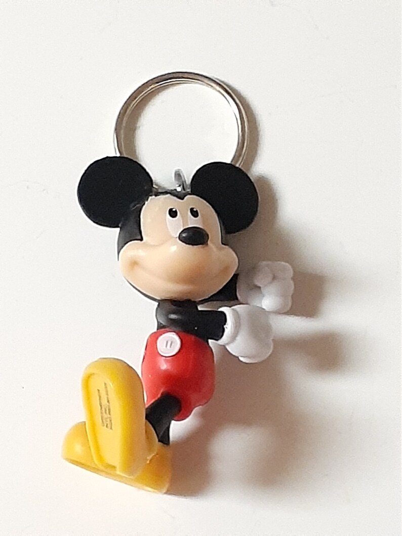 May include: A black and red Mickey Mouse keychain with a yellow shoe. The keychain has a silver metal ring.