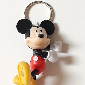 May include: A black and red Mickey Mouse keychain with yellow shoes. The keychain has a silver metal ring.