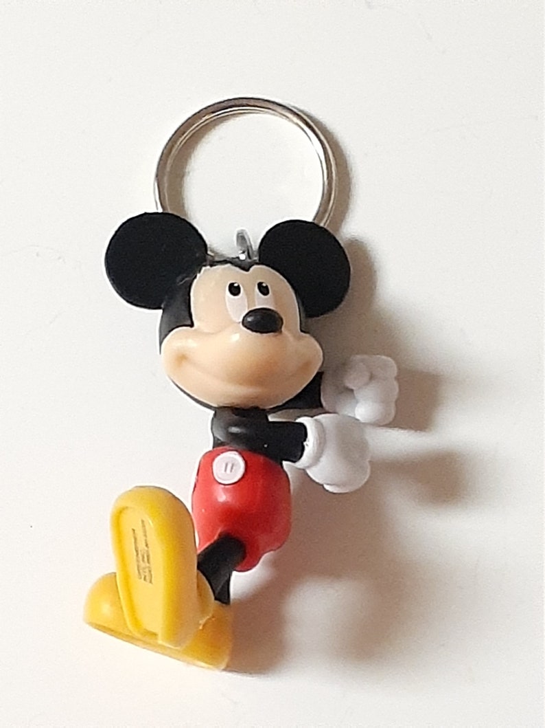 May include: A black and red Mickey Mouse keychain with yellow shoes. The keychain has a silver metal ring.