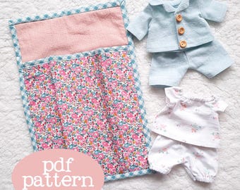 Puede incluir: Un patrón PDF para un saco de dormir para muñecas y dos conjuntos de pijamas. El saco de dormir es rosa y blanco con estampado floral. Los pijamas son azules y blancos con estampado floral. El texto "pdf pattern" está escrito en un círculo en la imagen.