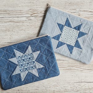 May include: Two rectangular zippered pouches featuring quilted fabric with a star-shaped centre design. The left pouch is dark blue with a floral pattern, while the right pouch is light blue with a small white floral print and a dark blue star.