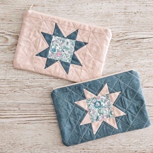 May include: Two quilted fabric pouches. One is pale pink with a blue star design and floral centre. The other is blue with a pink star design and floral centre. Both have a diamond pattern and a zip.