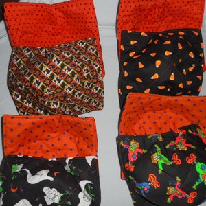 Op de afbeelding: Een verzameling gewatteerde komhoezen met Halloween-thema's. De hoezen hebben oranje stoffen met stippen en patronen met vleermuizen, geesten, snoepmaïs en vogelverschrikkers. De hoezen zijn ontworpen om kommen vast te houden en handen te beschermen tegen hitte.