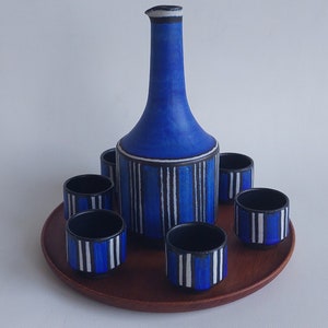 Peut inclure: Une carafe et six verres assortis en céramique bleu et blanc sur un plateau en bois. La carafe et les verres ont un motif rayé.