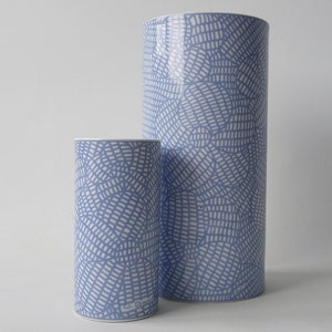 Könnte beinhalten: Zwei zylindrische Vasen in Blau mit weißem Kreuzschraffurmuster. Diese Keramikvasen eignen sich für die Inneneinrichtung. Die größere Vase ist etwa 30 cm hoch.