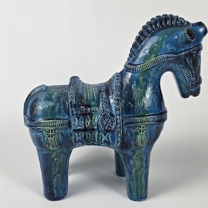May include: A ceramic horse figurine featuring a deep blue glaze with subtle green highlights. The sculpture displays intricate molded details on the saddle, harness, and mane, with a glossy finish that covers the entire surface of the animal.