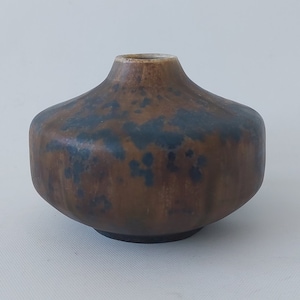 May include: A small, brown ceramic vase with a blue and brown glaze. The vase has a rounded body and a narrow opening.