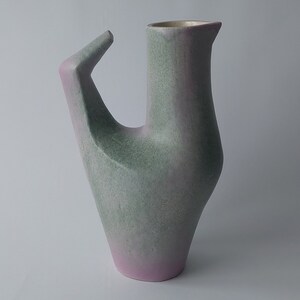 Puede incluir: Un jarrón de cerámica con un diseño abstracto único. El jarrón es de color verde claro y rosa con un acabado moteado.
