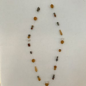 May include: A delicate necklace featuring a variety of beads in shades of brown, tan, gray, and white. The beads are strung on a clear, nearly invisible cord. The necklace has a simple, elegant design.