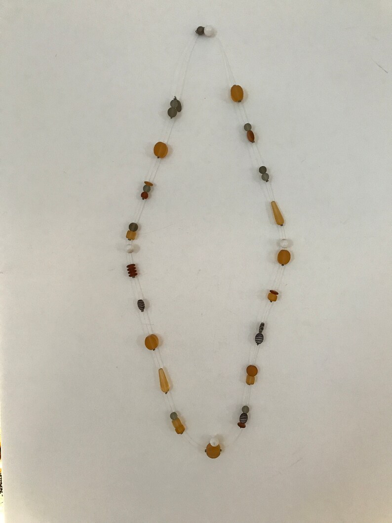 May include: A delicate necklace featuring a variety of beads in shades of brown, tan, gray, and white. The beads are strung on a clear, nearly invisible cord. The necklace has a simple, elegant design.