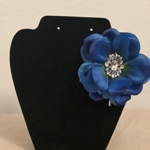 May include: A blue fabric flower with a rhinestone center, attached to a silver hair clip.