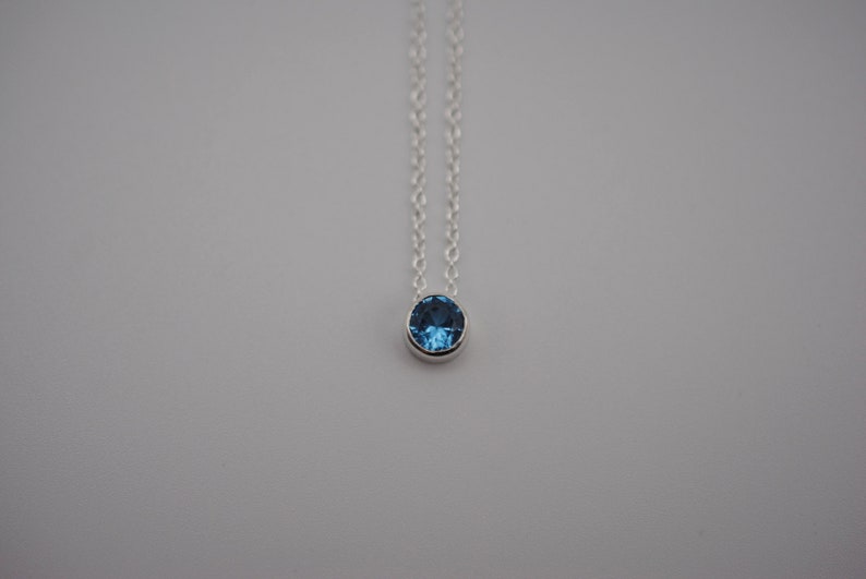 May include: A silver chain necklace with a small, round, blue gemstone pendant.