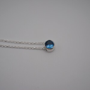 May include: A silver chain necklace with a small, round blue gemstone pendant.