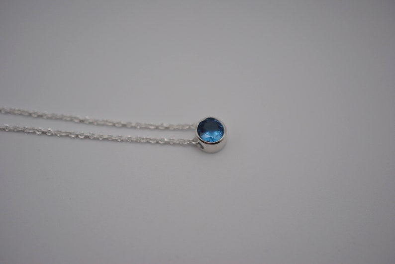 May include: A silver chain necklace with a small, round blue gemstone pendant.