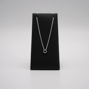 May include: A silver chain necklace with a small, round, dark blue gemstone pendant.