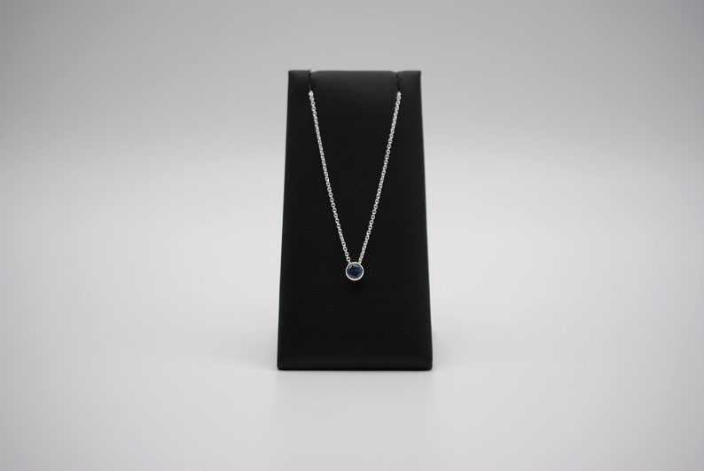 May include: A silver chain necklace with a small, round, dark blue gemstone pendant.