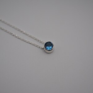 May include: A silver chain necklace with a small, round blue gemstone pendant.