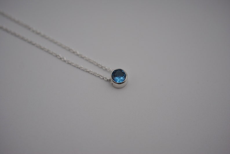 May include: A silver chain necklace with a small, round blue gemstone pendant.