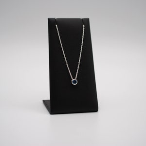 May include: A silver chain necklace with a small, round, dark blue gemstone pendant.