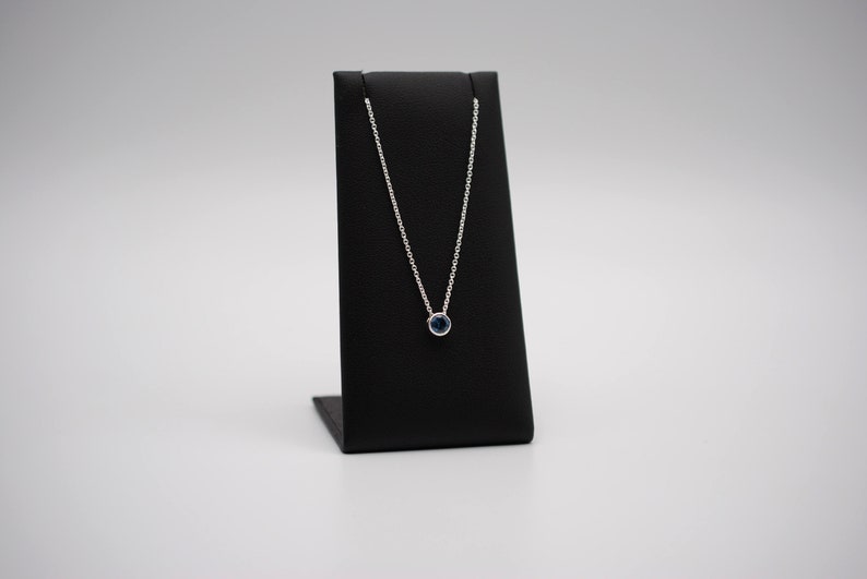 May include: A silver chain necklace with a small, round, dark blue gemstone pendant.