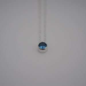 May include: A silver necklace with a small, round blue gemstone pendant.