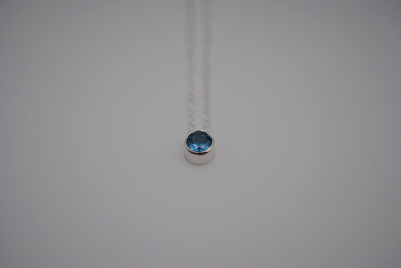 May include: A silver necklace with a small, round blue gemstone pendant.