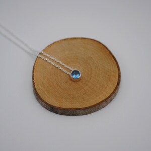 May include: A silver chain necklace with a small, round blue gemstone pendant.