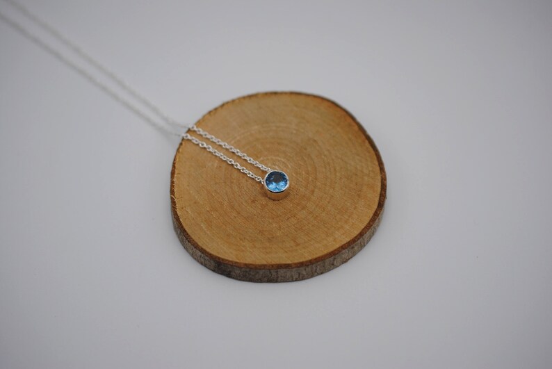 May include: A silver chain necklace with a small, round blue gemstone pendant.