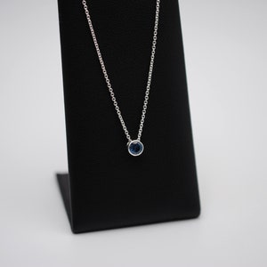 May include: A silver chain necklace with a small, round, blue gemstone pendant.
