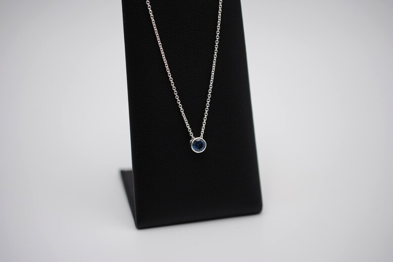 May include: A silver chain necklace with a small, round, blue gemstone pendant.
