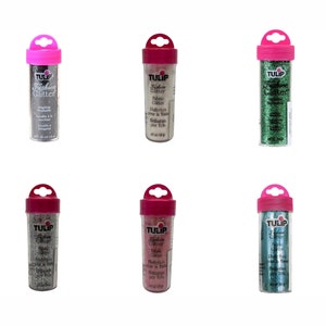 May include: Six small bottles of Tulip Fashion Glitter in various colors, including silver, gold, green, pink, and blue. Each bottle has a pink lid with a handle and a clear plastic body.