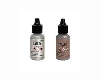 May include: Two small bottles of Alloy ink, one silver and one rose-colored, each with a black cap. The silver bottle is labeled "Sterling," and the rose bottle is labeled "Rose." Both bottles have hazard symbols and the text "Danger Flammable!" and are 5 fl oz.