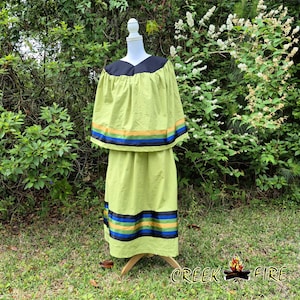 May include: A lime green dress and cape set with black trim and colorful stripes. The cape has a black neckline. The dress and cape are displayed on a mannequin. The text "CREEK FIRE" is visible in the lower right corner.