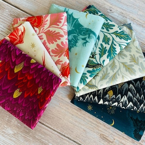 May include: A collection of seven folded fabric swatches arranged in a fan shape. The patterns include red and purple dragon scales, cream with red dragons, pink and white foliage, light blue with dragons, teal leaves, white with gold leaves, and black with white scales and gold stars.