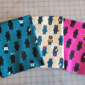 May include: Three fabric panels with a repeating pattern of black bears wearing different accessories. The panels are teal, cream, and pink.