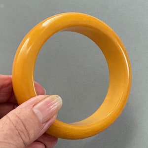 May include: A yellow plastic bangle bracelet. The bracelet is smooth and shiny.