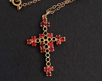 May include: A gold chain necklace with a red jeweled cross pendant. The cross is made of small red stones set in a gold frame.