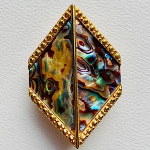 May include: Abalone shell pendant in a diamond shape, framed with gold-colored metal. The iridescent shell displays a mix of colors, including blue, green, and brown. The gold frame has a beaded edge, adding a decorative touch.