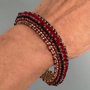 May include: A multi-strand beaded bracelet with red, black, and silver beads. The bracelet is wrapped around a person's wrist.