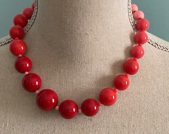 May include: A red and pink ombre beaded necklace with large round beads. The necklace is on a mannequin bust.