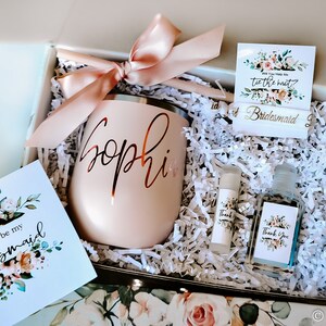 May include: A blush-coloured gift box containing a personalised tumbler, cards, and small bottles. The tumbler is inscribed with "Sophie" in a cursive font. The box includes cards that say "Will you be my bridesmaid?" and "Thank You".