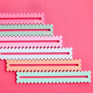 May include: A collection of colorful, scalloped-edge organizers in shades of pink, mint green, white, and peach, arranged on a vibrant pink background. Each organizer has a rectangular opening and the name "Tanya" in a script font.