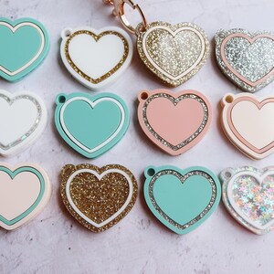 May include: Ten heart-shaped keychains with various designs. Some are solid colors, while others have glitter or a sparkly finish. The keychains are all in the shape of a heart.