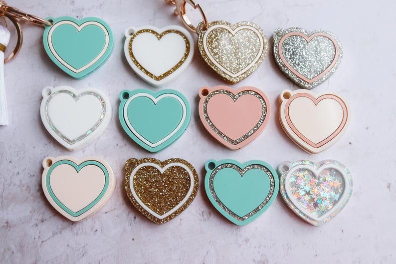 May include: Ten heart-shaped keychains with various designs. Some are solid colors, while others have glitter or a sparkly finish. The keychains are all in the shape of a heart.