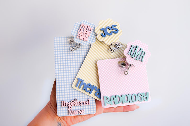 Puede incluir: Tres portatarjetas rectangulares con patrones de cuadros vichy en azul, amarillo y rosa. Cada uno tiene un adorno festoneado con textos como "faith over fear", "JCS" y "KMR". El azul dice "Registered Nurse", el amarillo "Therapy" y el rosa "RADIOLOGY".